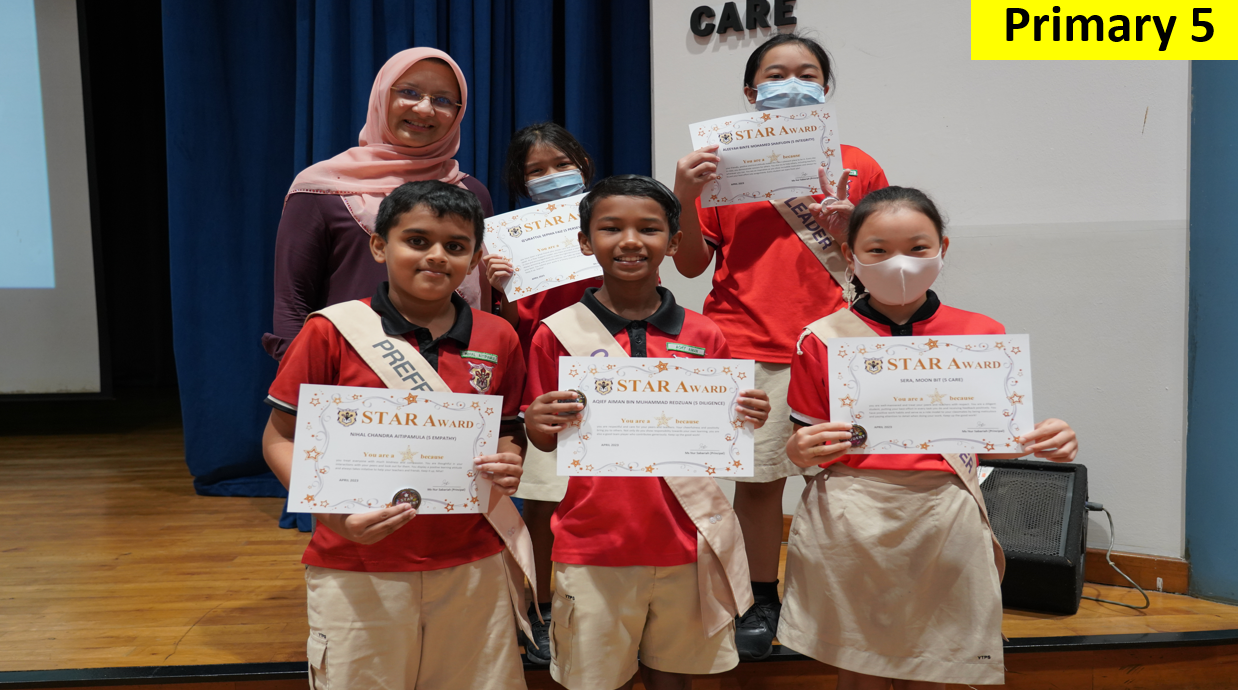 Five Primary 5 students in red uniforms hold Star Award certificates, standing with a teacher wearing a pink hijab.